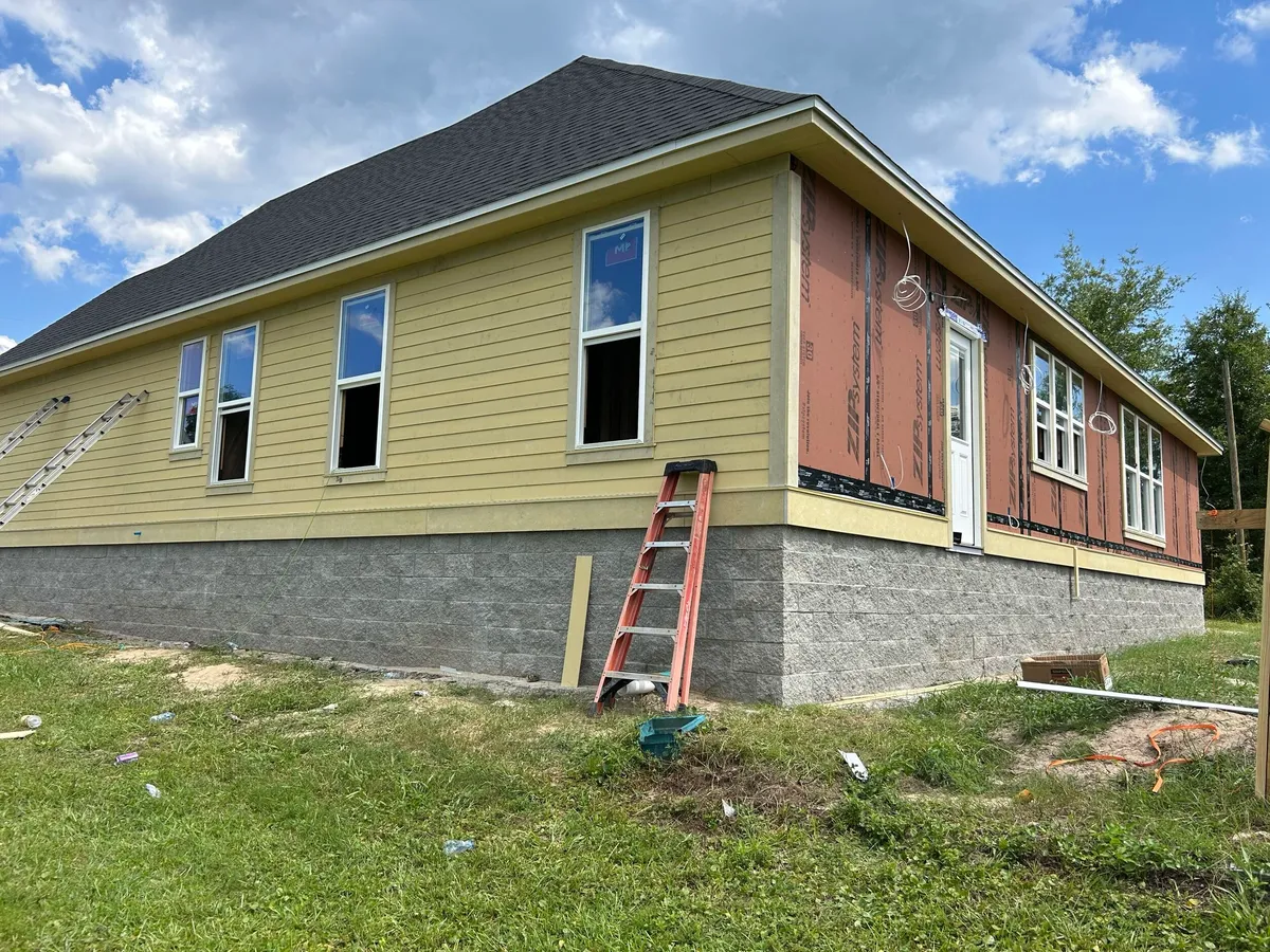 Long side of the house with unpainted yellow lap siding partly installed above the split-face stemwall.