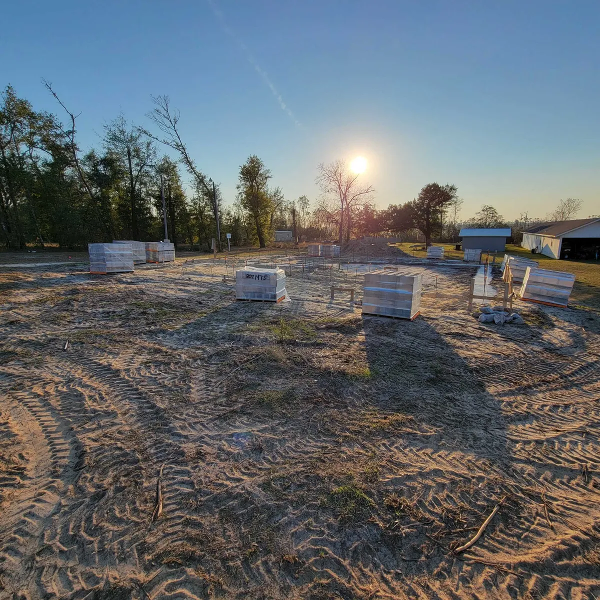 Cleared building site with pallets of concrete block, photographed into the sun.