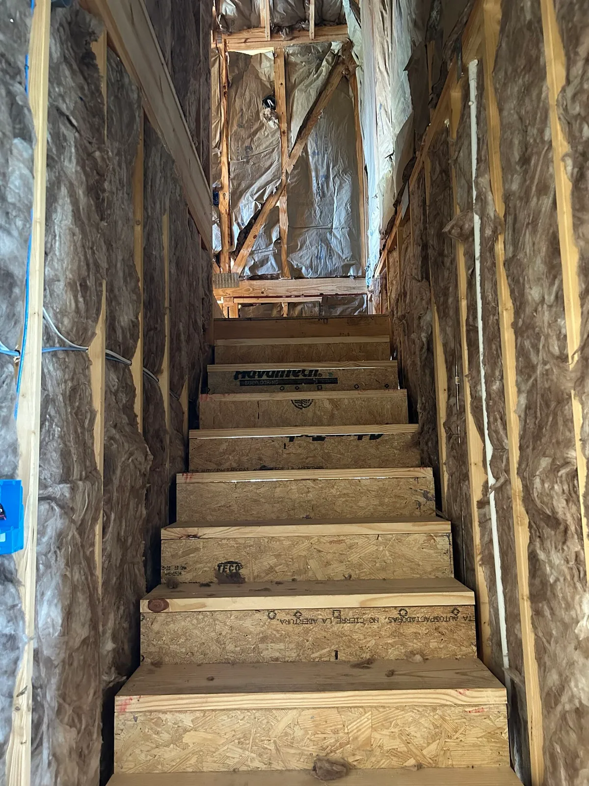 Stair enclosure with batt insulation between the wall studs and temporary treads.