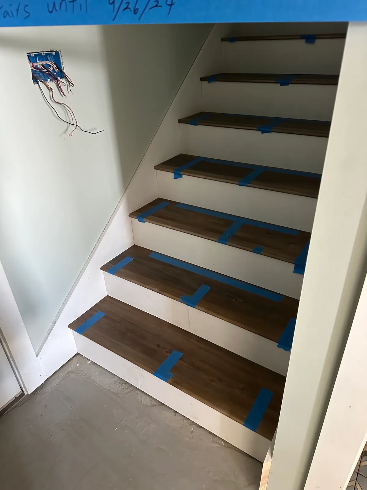Stair with stained treads and white risers, protected by painter’s tape.