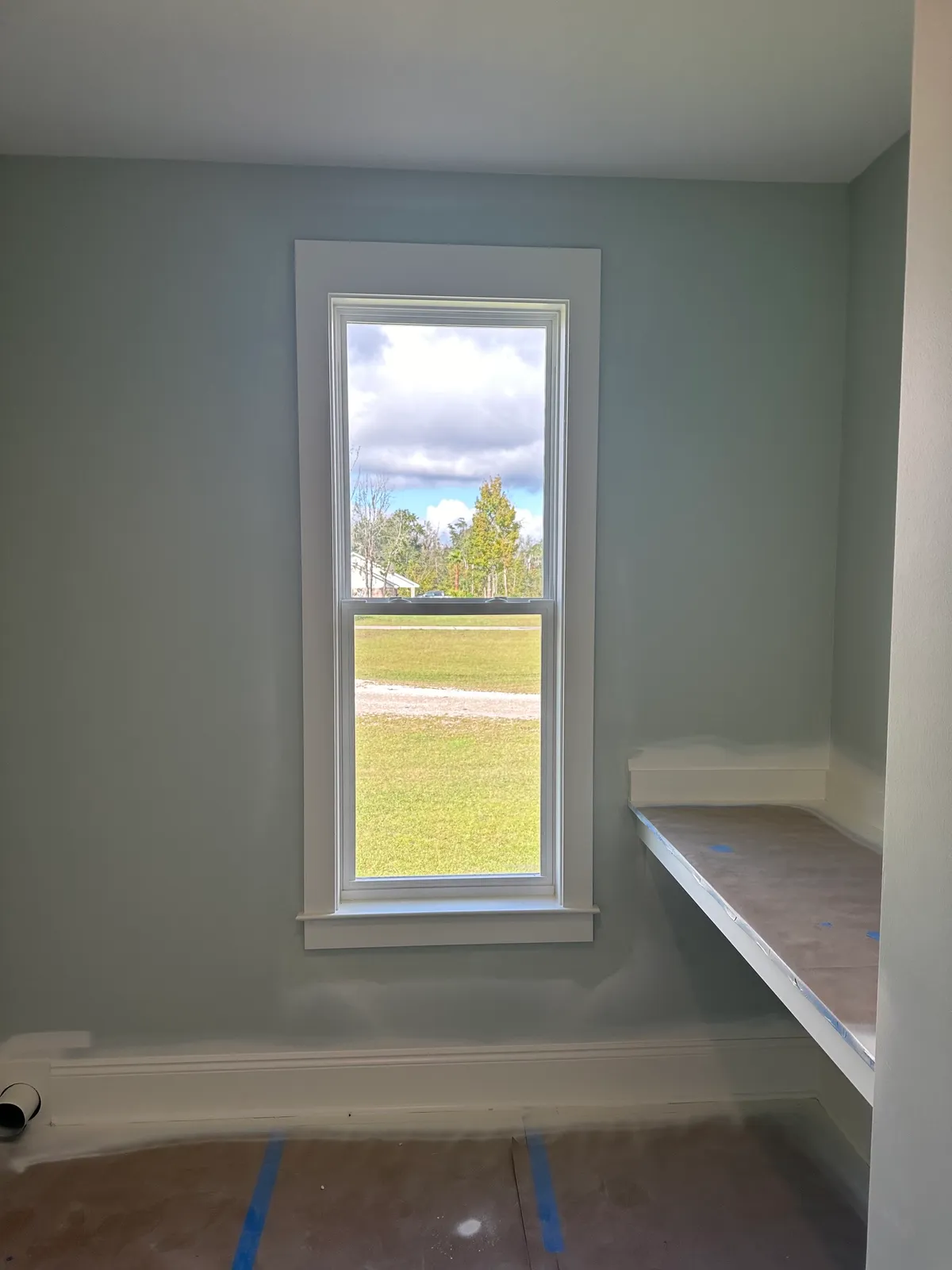 Room with a single tall window and a built-in shelf, with protective covering on the floor.