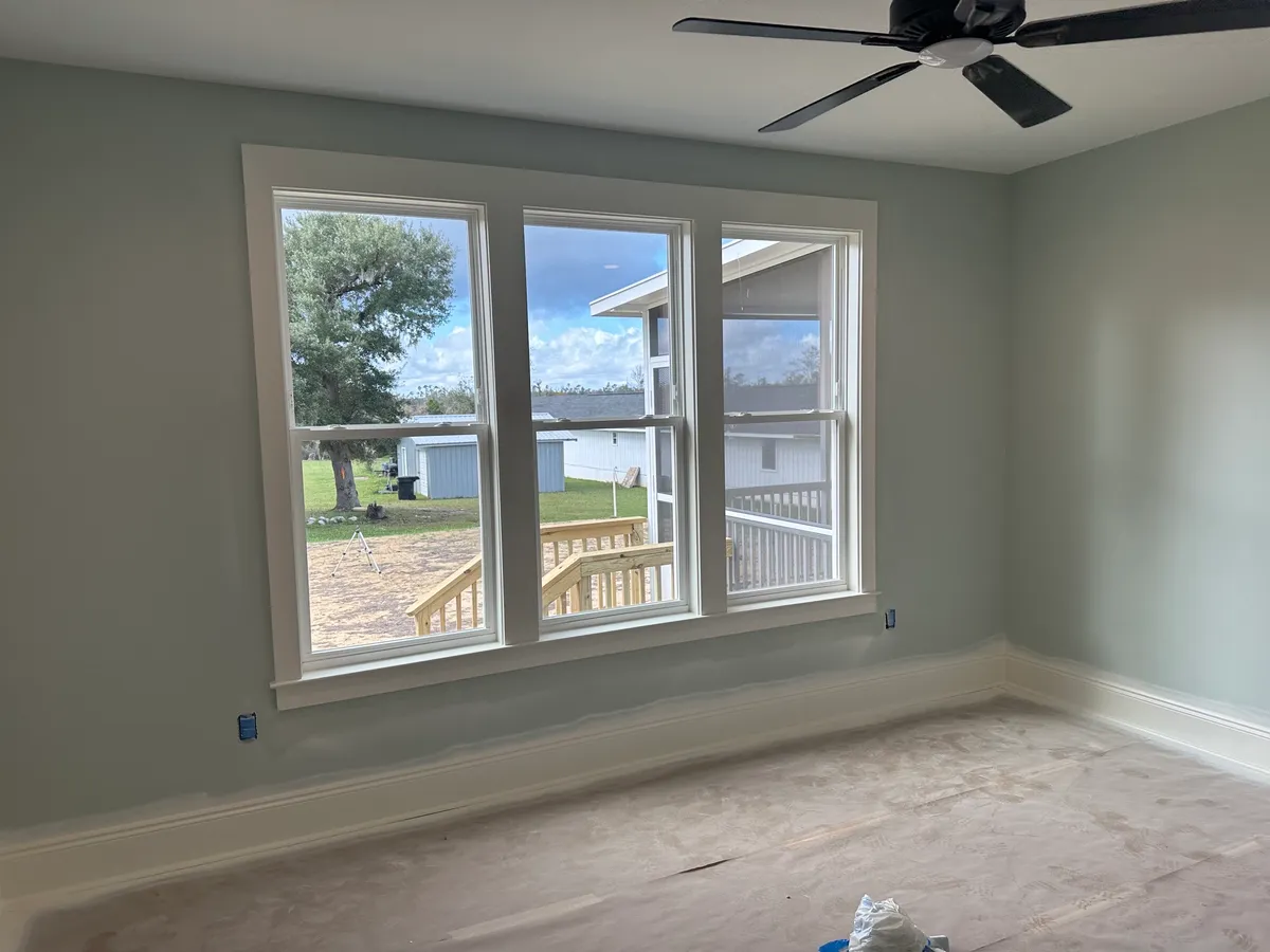 Room with a triple window, ceiling fan, and baseboards, with protective paper on the floor.