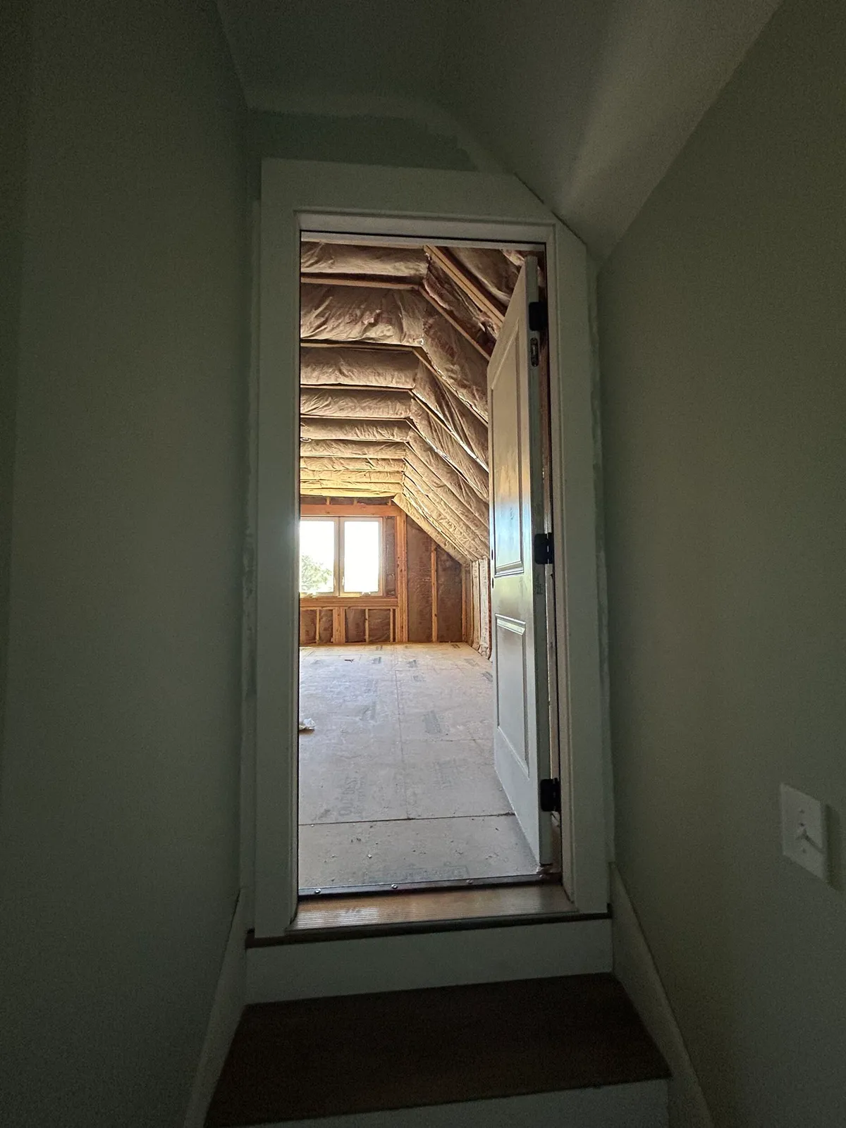 View up a step through a doorway into an upstairs space with exposed insulation and framing.