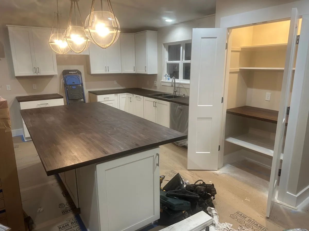 Kitchen during finishing, with a wood countertop on the island, an open pantry, and tools on the floor.