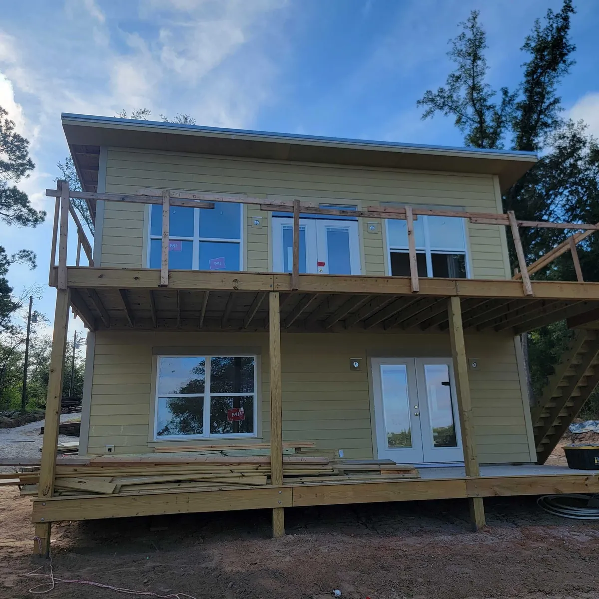 Lake-facing side in primed siding with the upper deck framed and temporary railings, before finish work.