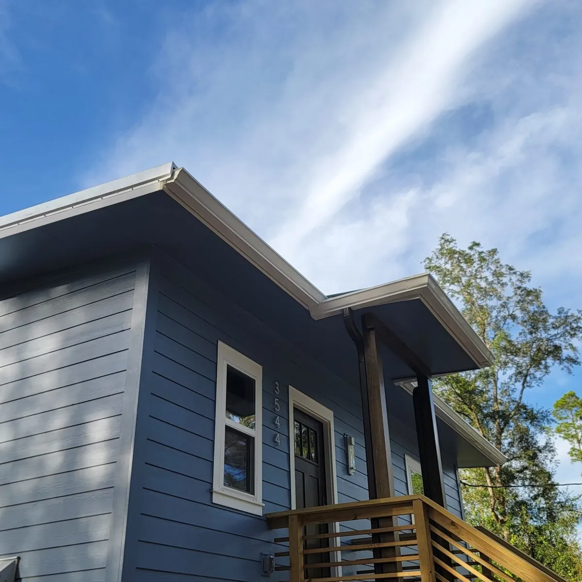 Covered upper entry with a shed roof on wood posts and a horizontal-board railing, against blue siding and sky.