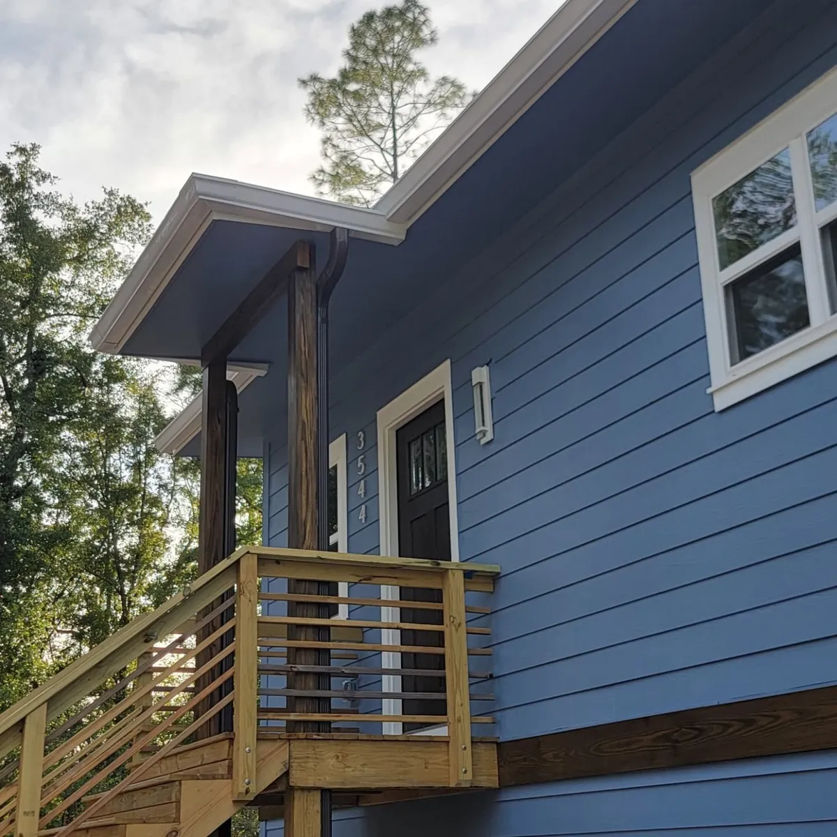 Unstained wood entry stair and horizontal railing below the covered upper entry.