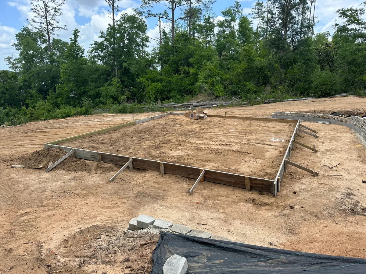 Wood forms outlining the foundation on a cleared, graded site with trees behind.