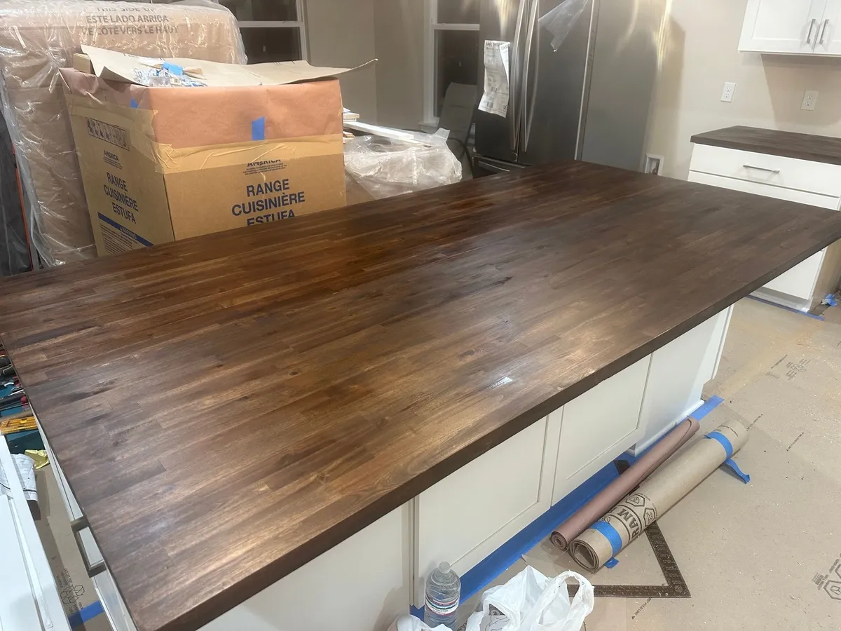 Large dark wood countertop on the white kitchen island, with protective paper on the floor.