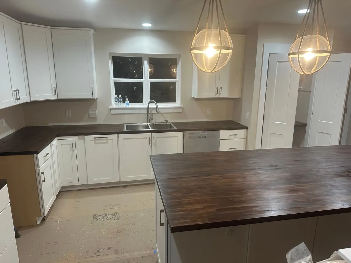White cabinets and dark wood countertops along the sink wall, with the island countertop in the foreground.
