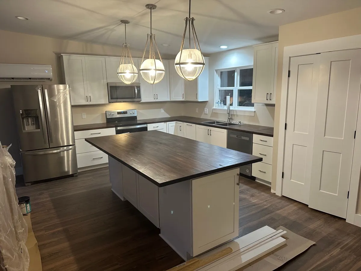 Kitchen with white cabinetry, a wood-topped island under three globe pendants, stainless appliances, and a double-door pantry.