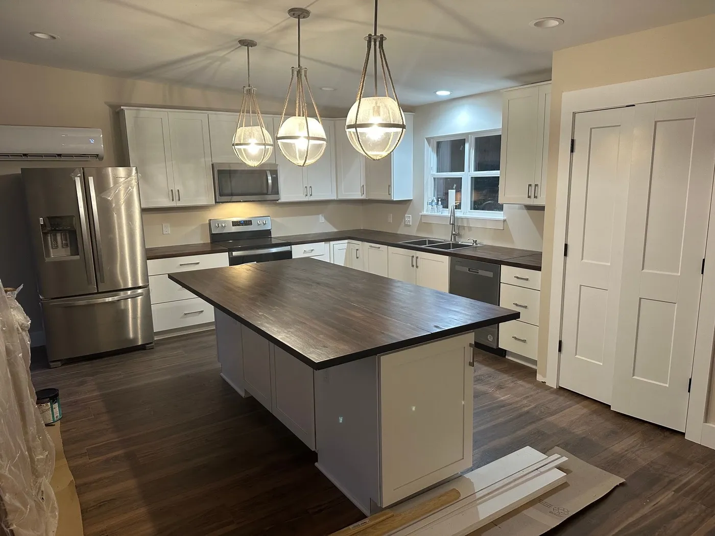 Kitchen with white cabinetry, a wood-topped island under three globe pendants, stainless appliances, and a double-door pantry.