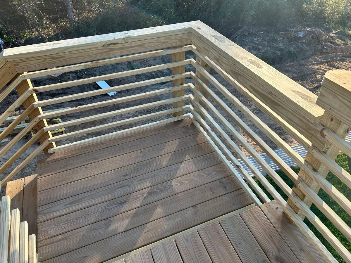Corner of an unstained wood landing with horizontal railings, seen from above.