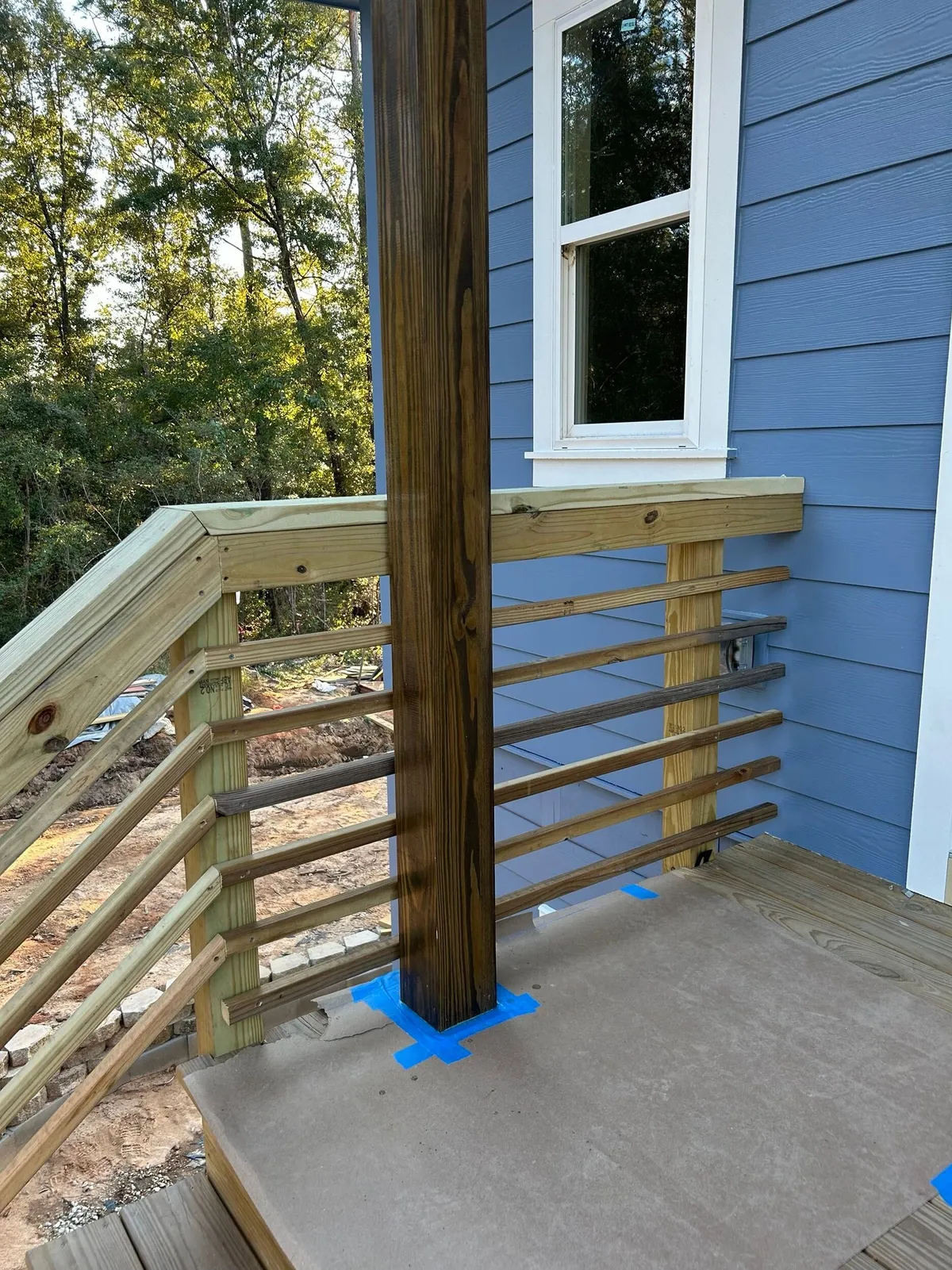 Wood porch post and horizontal railing on a landing beside blue siding.