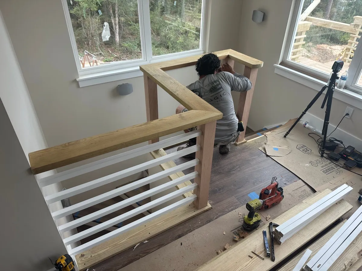 A worker setting the wood cap on the stair railing, with rails and tools laid out nearby.