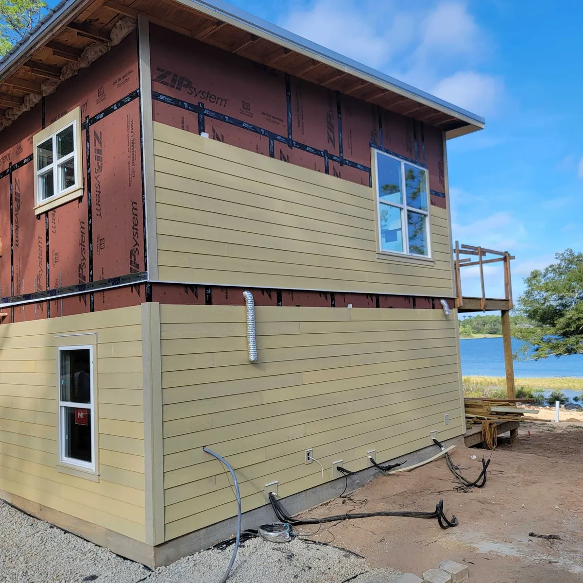 Two-story home with lap siding installed on the lower walls and partly on the upper walls over red sheathing.