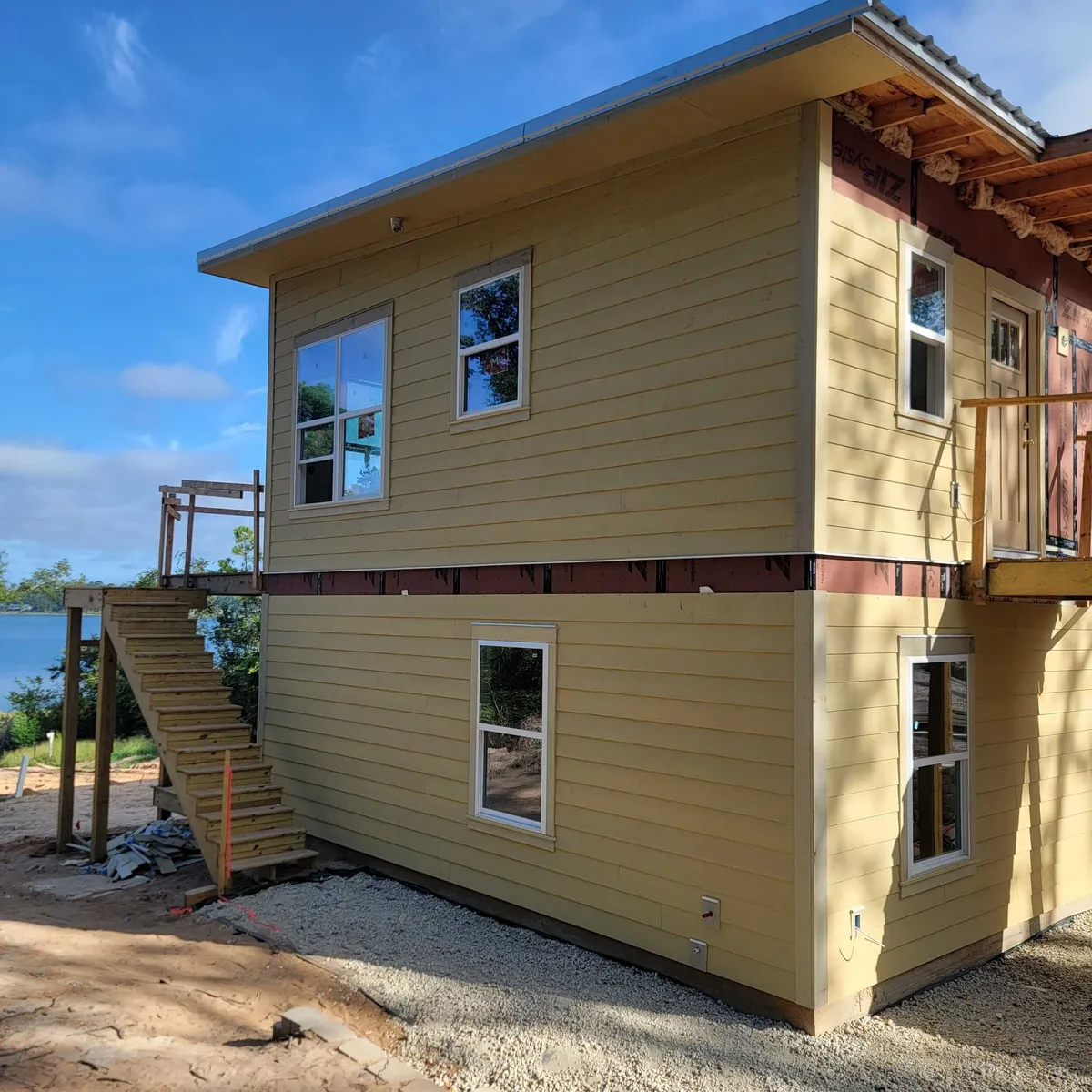 Side of the home in primed lap siding, with the exterior stair framed at left and the lake beyond.