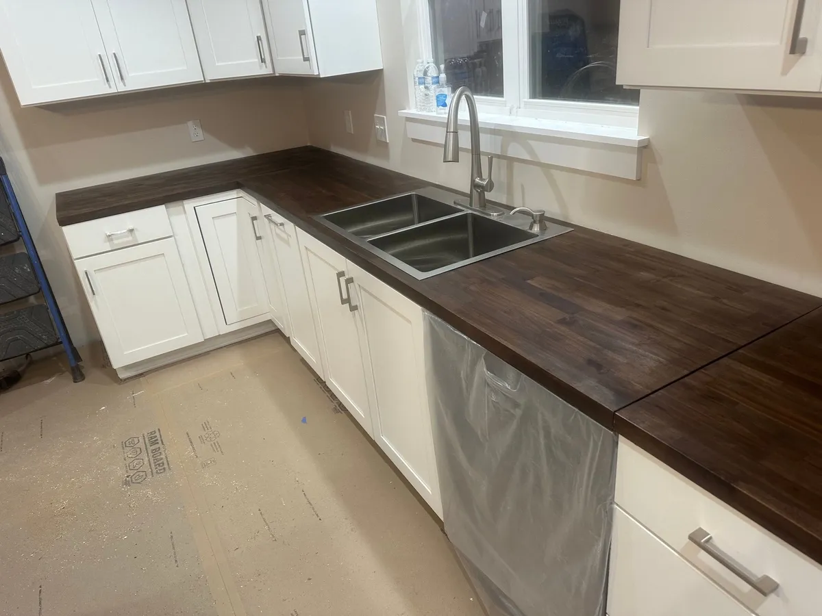 Wood countertops installed along white base cabinets, with a stainless sink and dishwasher.