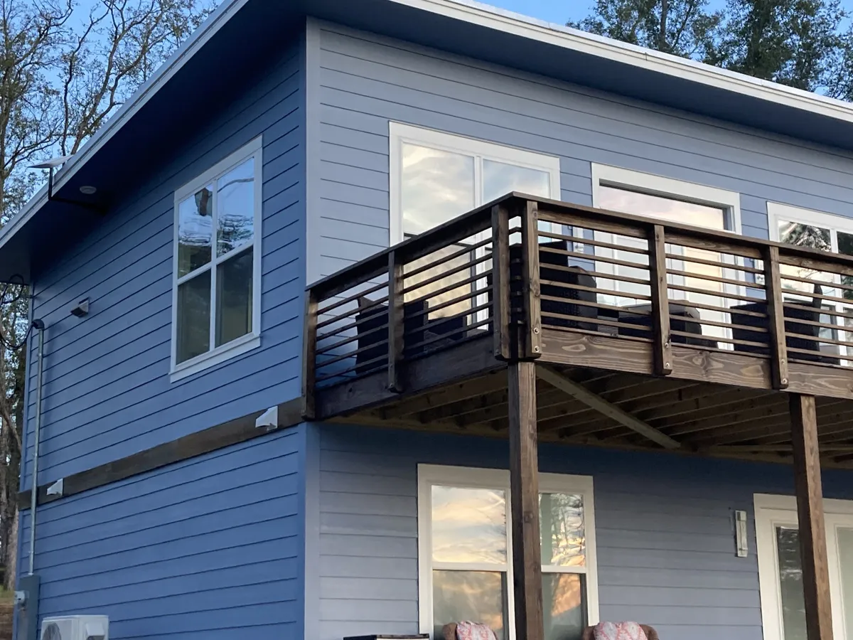 Upper deck with stained posts and horizontal wood railings against the blue siding.
