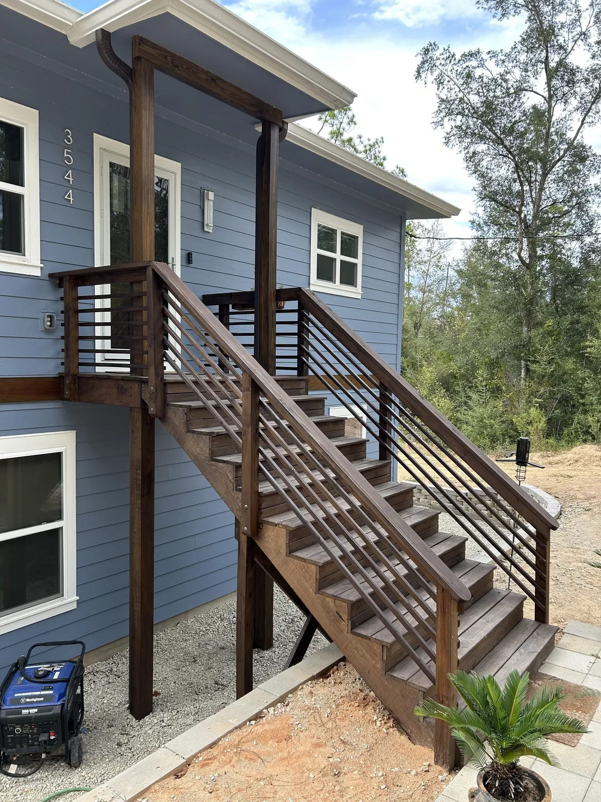 Stained wood entry stairs with horizontal railings rising to a covered upper entry on the blue-sided home.