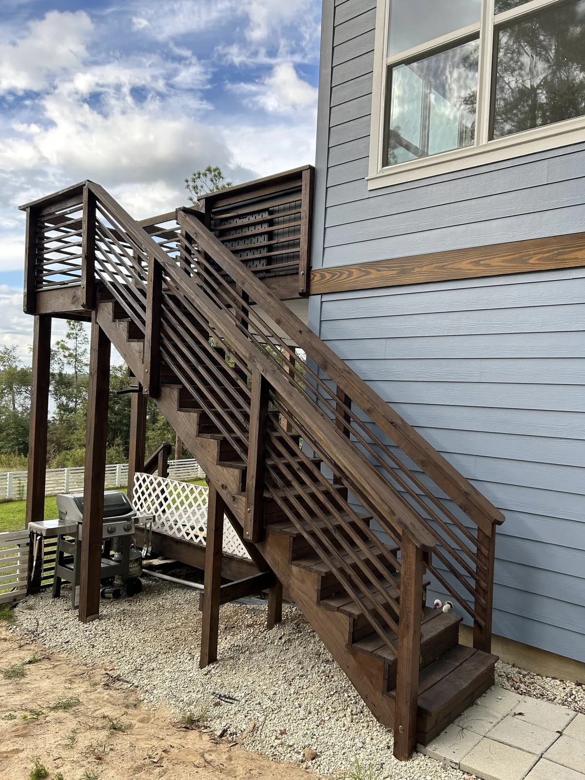 Stained exterior stairs with horizontal railings climbing the side of the home to an upper landing.