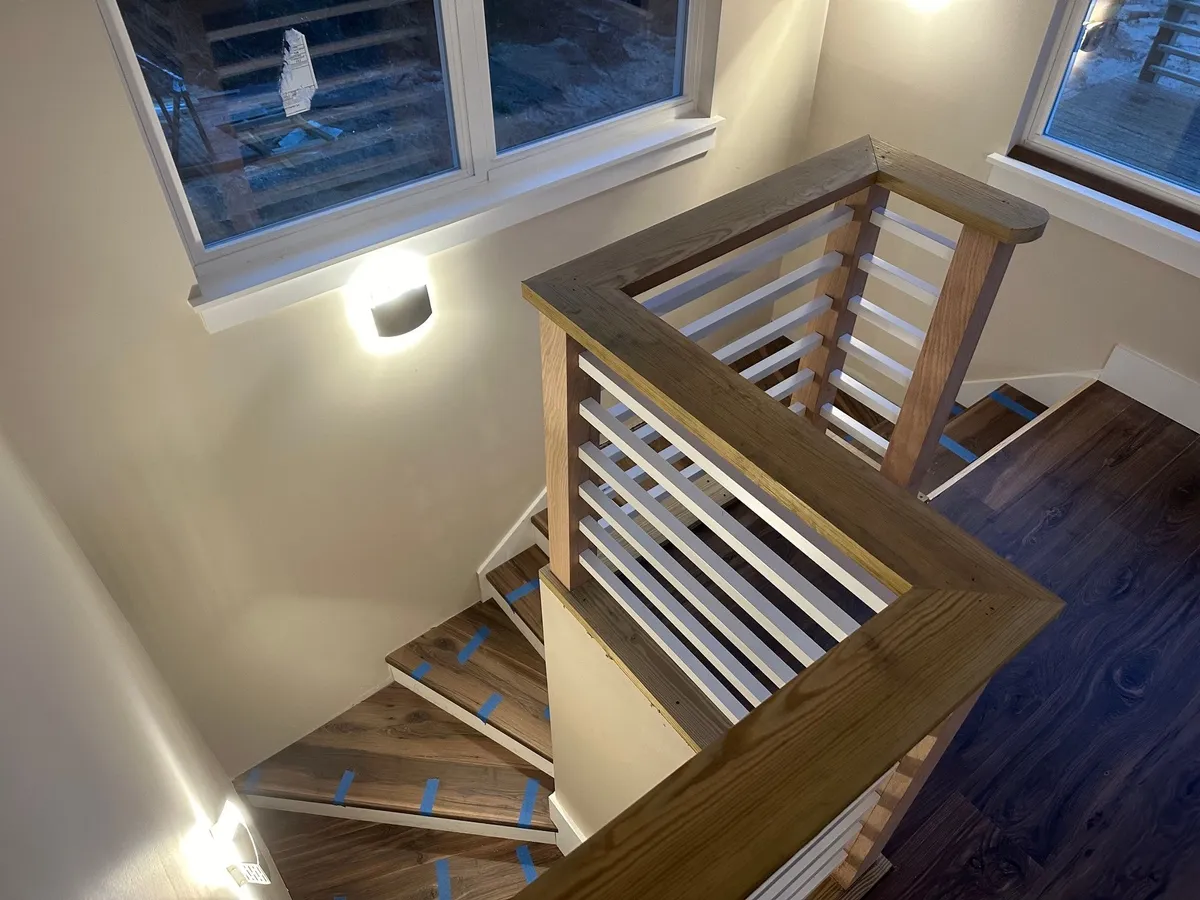 Looking down past the wood railing cap to stair treads still marked with tape.