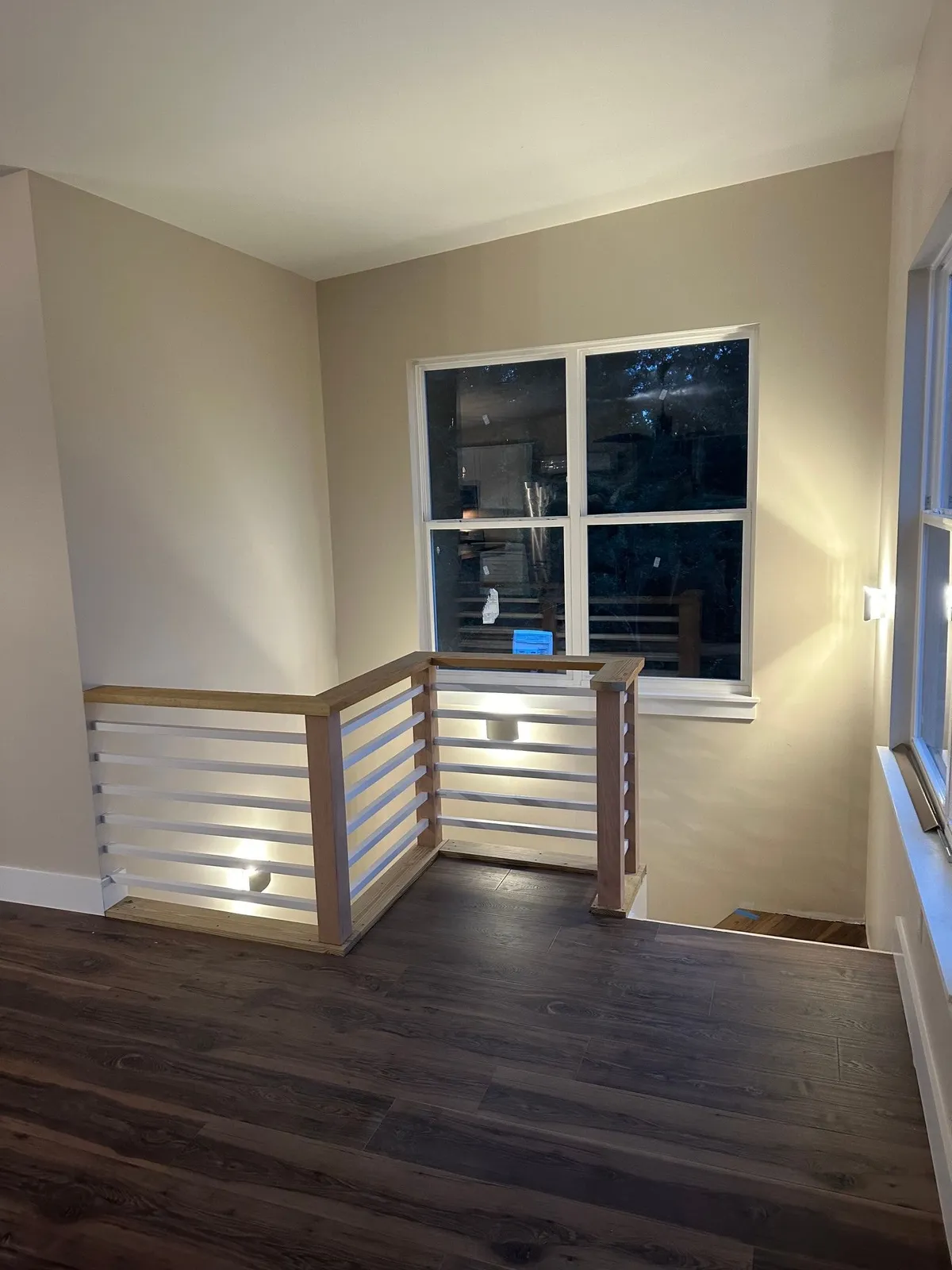 Upstairs landing with a white horizontal railing and wood cap around the stair opening, beside a window.