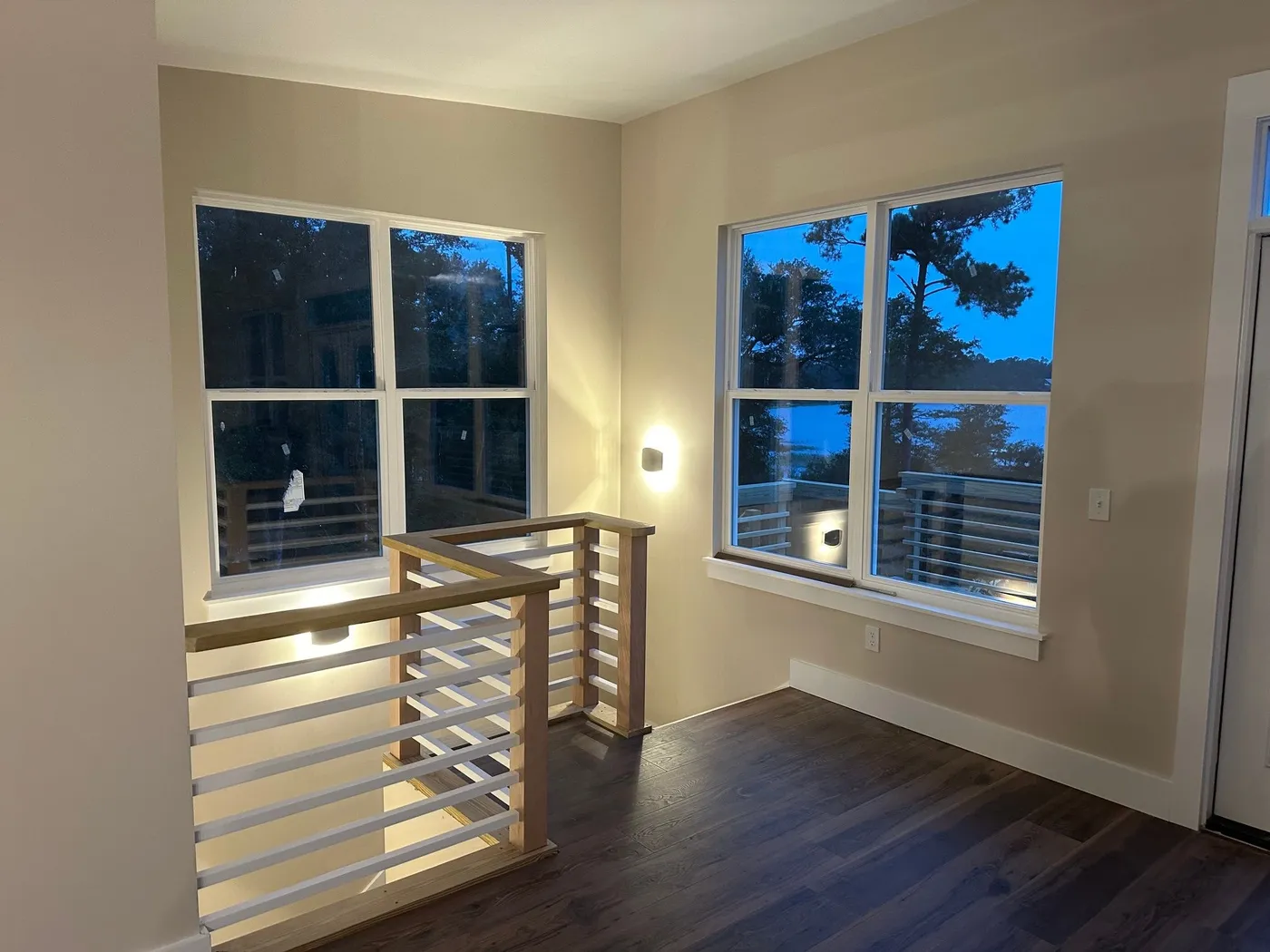Stair opening framed by wood posts and a wood cap with white horizontal rails, in a corner with two windows.