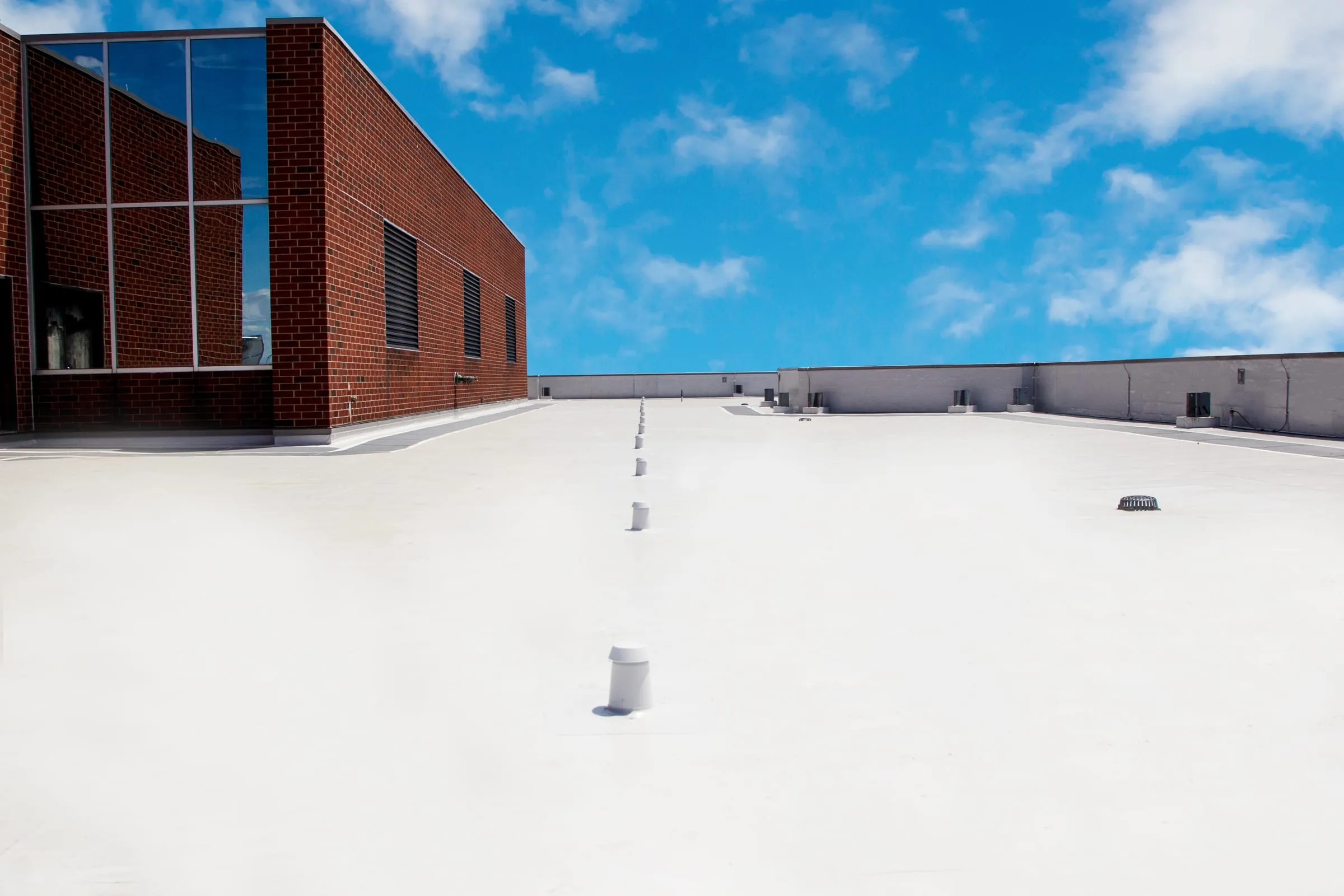 A white single-ply membrane roof covering a large low-slope commercial roof beside a brick building.
