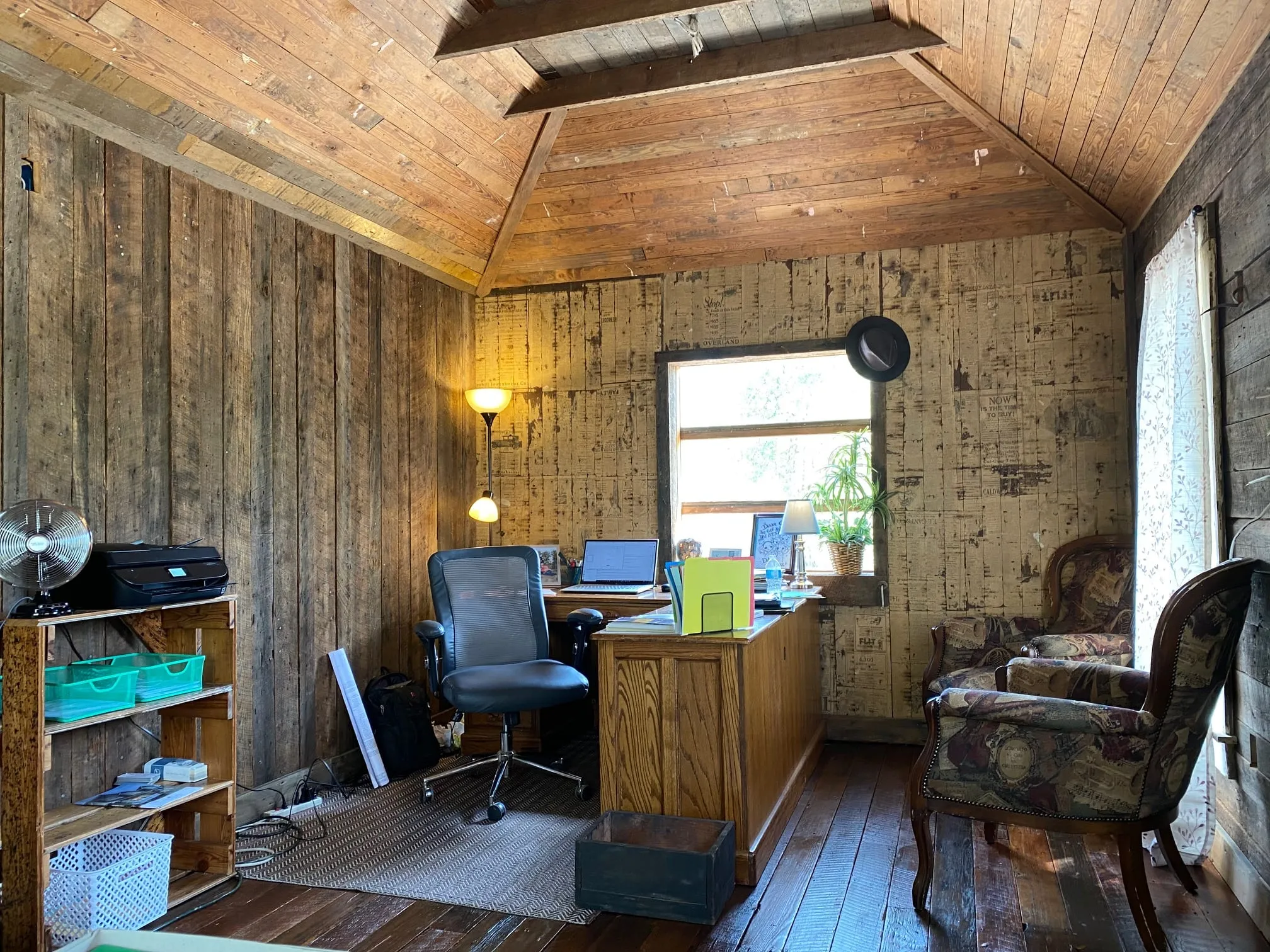 Guy's office with exposed ceiling beams, wood walls, plank flooring, and a desk beneath the window.