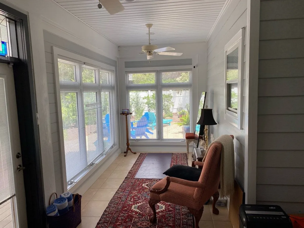 Enclosed porch before the remodel, with rows of windows, a tile floor, a runner rug, and an armchair.