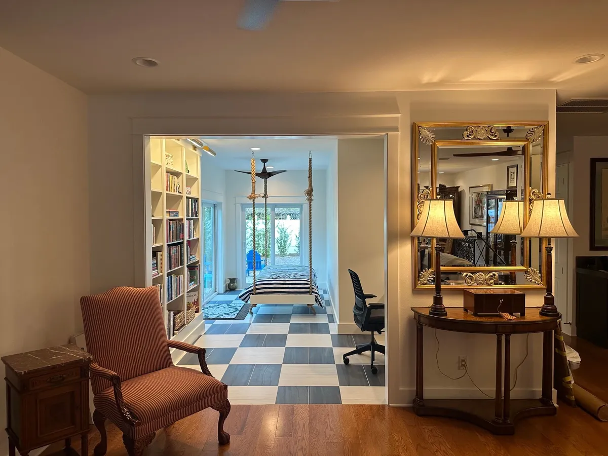 View from the living room through a wide trimmed opening into the remodeled room, with the bookcase and hanging bed beyond the checkerboard floor.