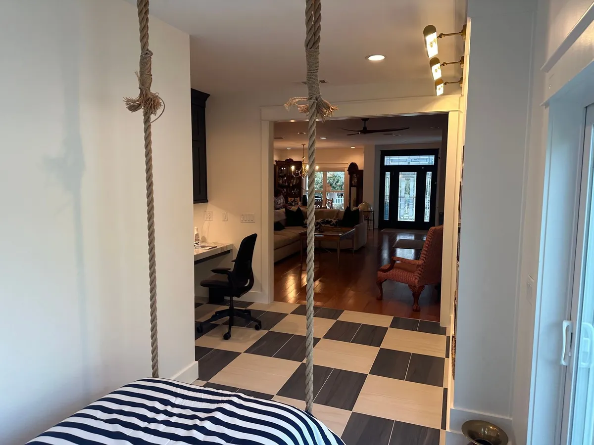 View past the hanging bed's ropes toward the desk area and an opening into the main house.