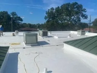 Broad view of the white membrane roof with rooftop units, a cord, and a green metal roof section.