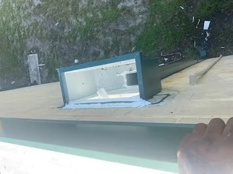 Looking down over the roof edge at a drainage collector box on the gutter, with grass below.