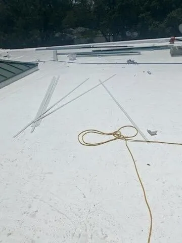 Metal strips and a cord laid across the white membrane, with the roof edge and trees beyond.