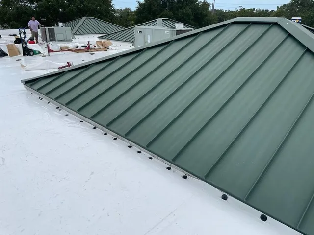 White membrane along the base of green standing-seam metal roof sections.