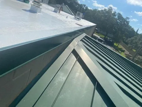 The membrane edge above a green standing-seam metal roof section, seen from the roof.
