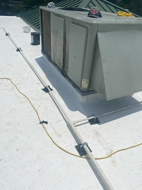 A rooftop unit on support rails over the white membrane, with a cord across the roof.