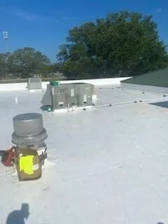 A vent penetration on the membrane with a tool beside it and a rooftop unit beyond.