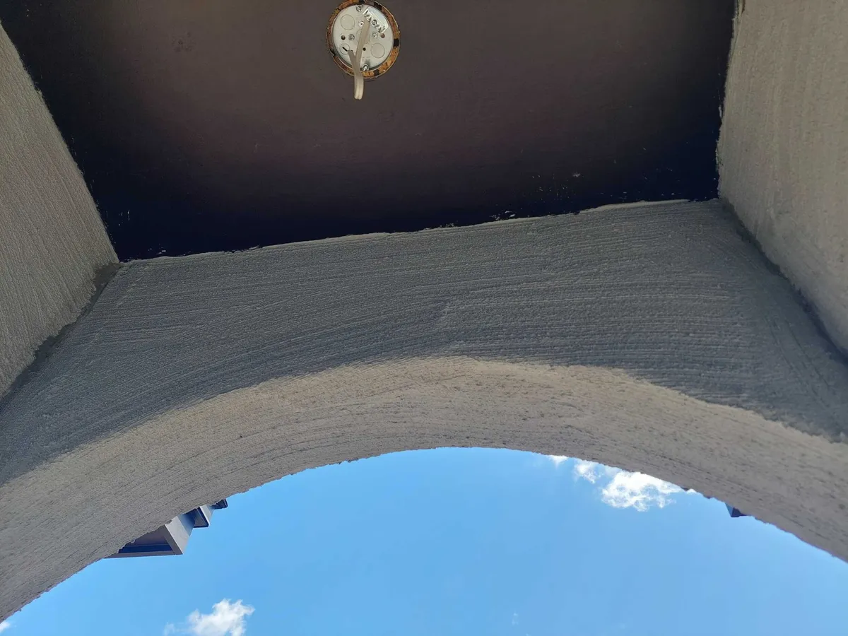 Looking up through the stuccoed entry arch toward the dark soffit and a light fixture box.