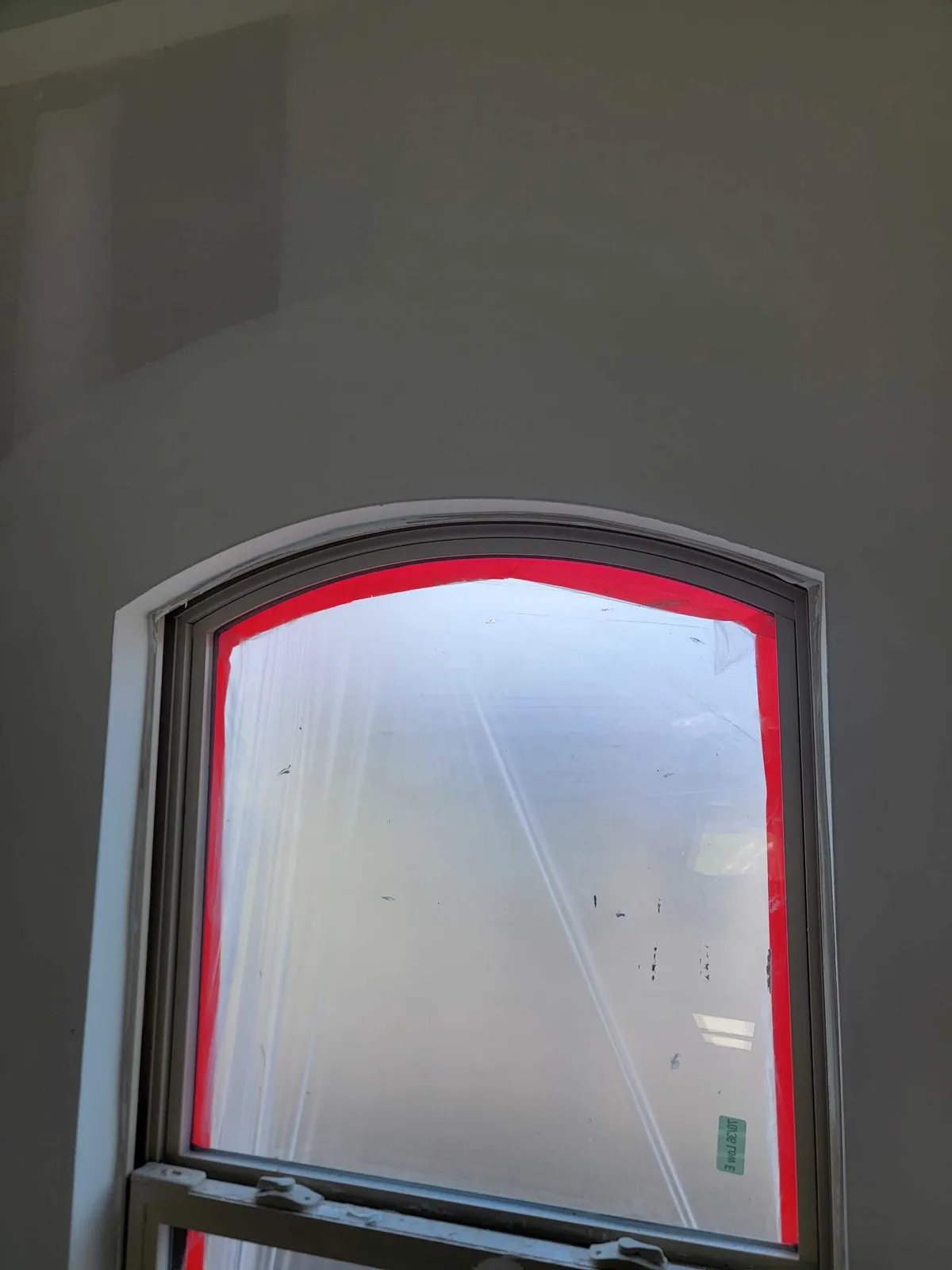 Arched window in its drywall reveal, covered with protective film during interior work.