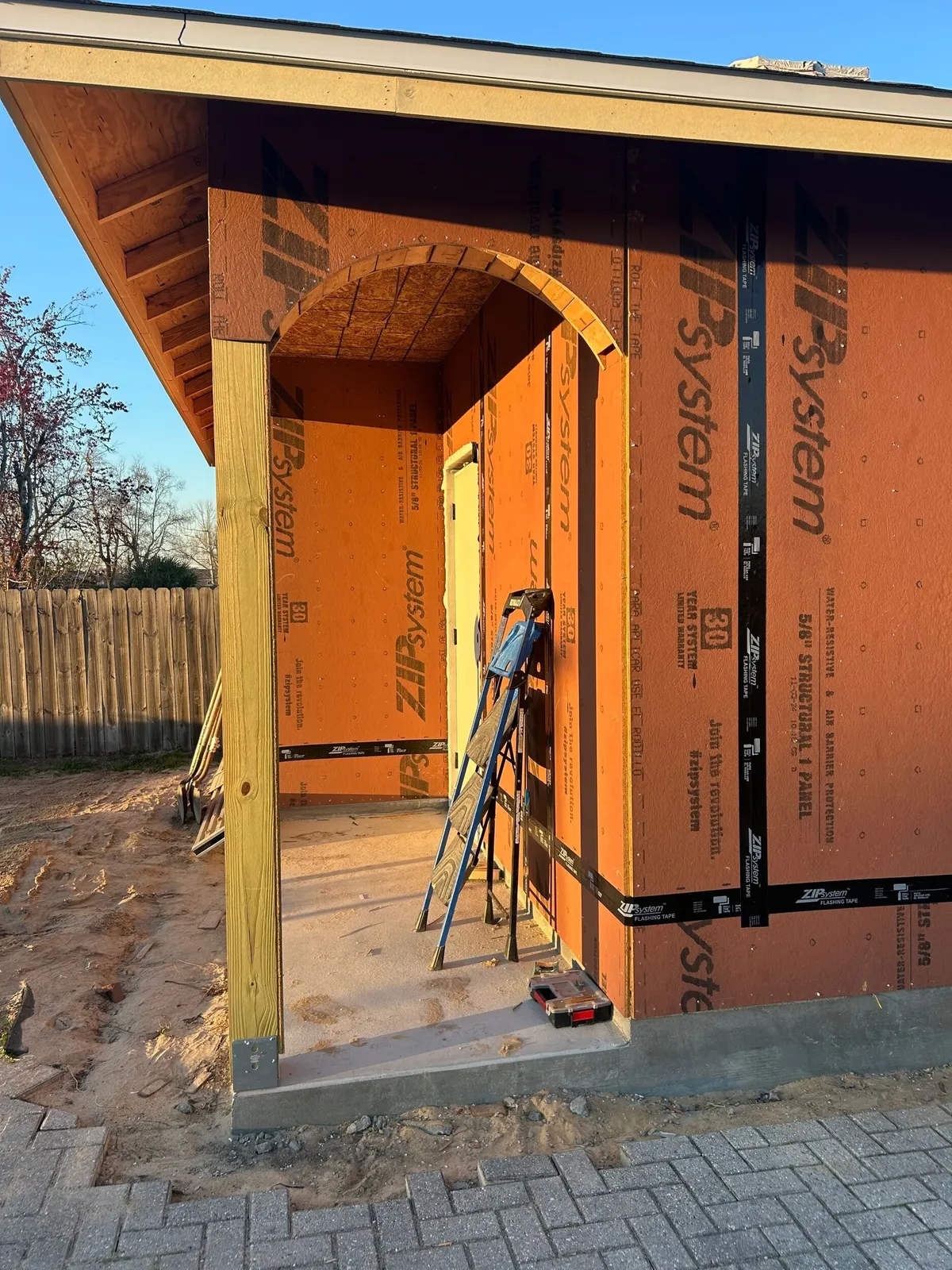 Sheathed back porch with a framed arch overhead and a wood post at the corner.