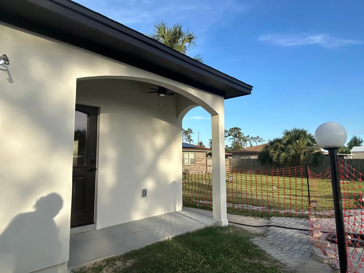 Arched back porch with a dark door and a ceiling fan, a globe lamp post in front, and orange safety fencing in the yard.