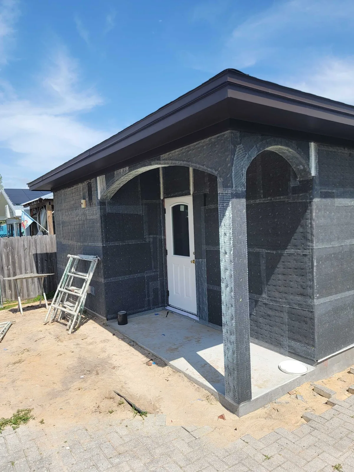Back porch with lath on the walls, arches, and columns, and a white door.