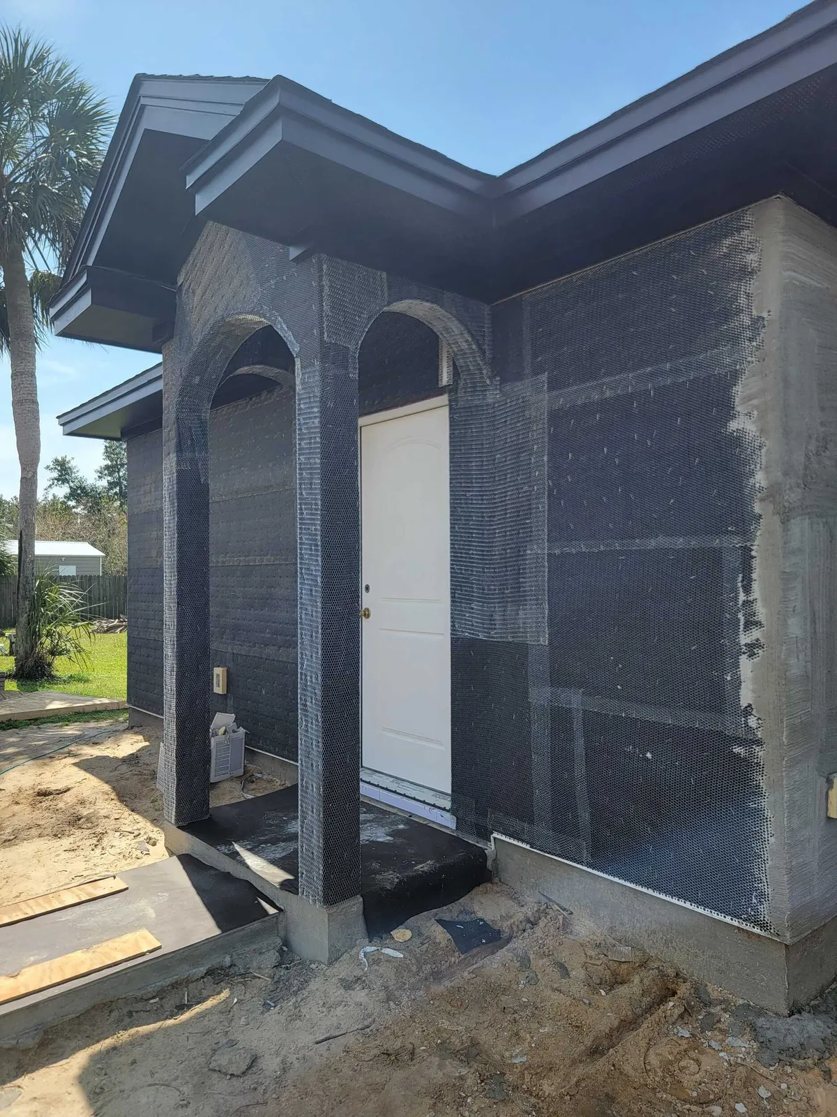 Porch arches and walls covered in dark building paper and metal lath, ready for stucco, around a white door.