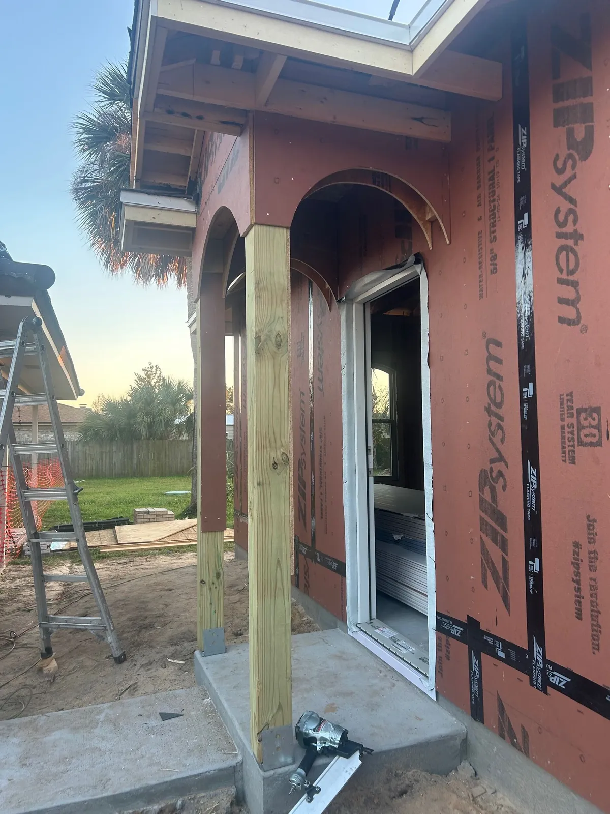 Back porch corner with framed arches, a wood post, and the back door installed in the sheathed wall.
