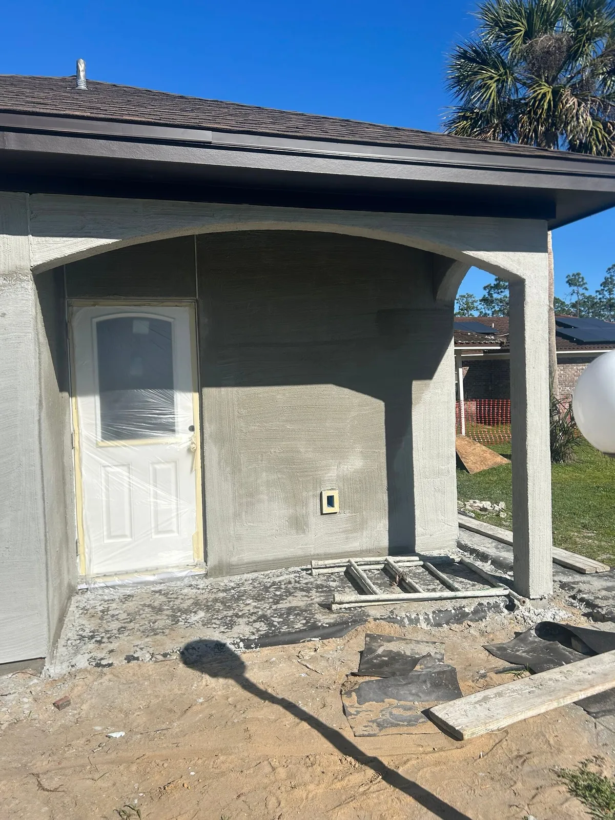 Porch with stucco walls and arch around a white door, with materials still on the ground.