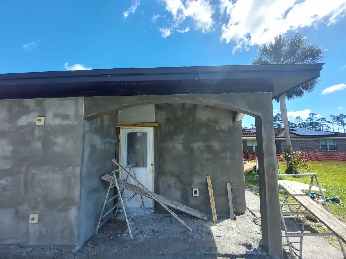 Back porch with stucco applied to the walls and arch, with a ladder and planks in front.