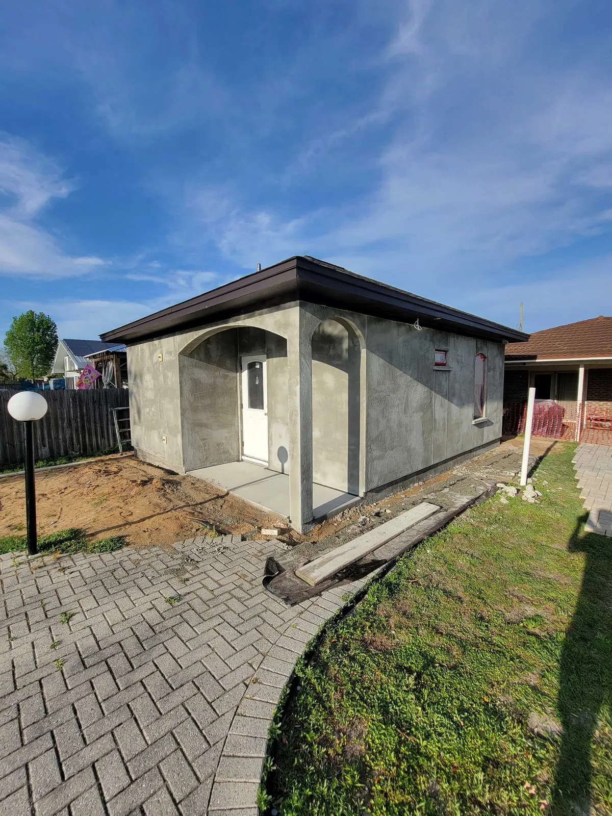 The studio after stucco, with the arched porch, a white door, a globe lamp post, and a paver walk.